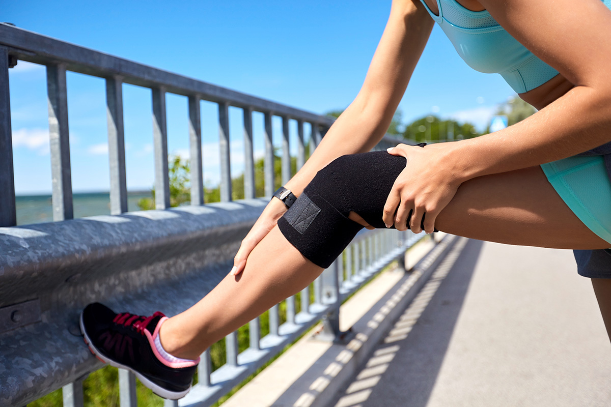 fitness, sport and healthy lifestyle concept - close up of young woman in knee brace stretching leg outdoors