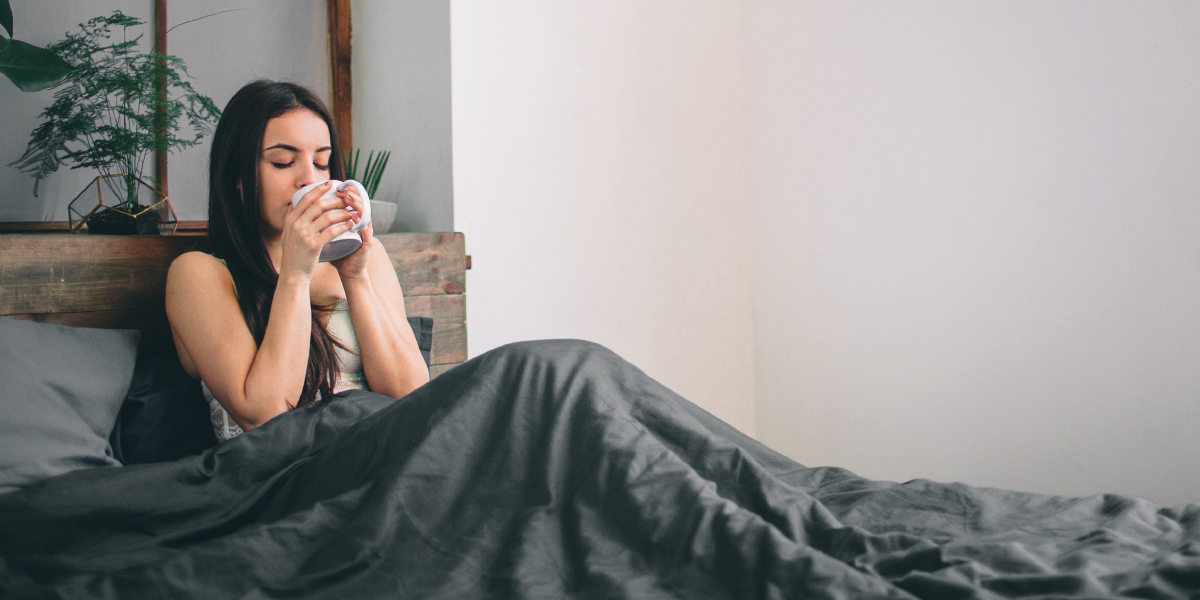 mulher sentada na cama tomando um chá para dormir melhor, qualidade do sono